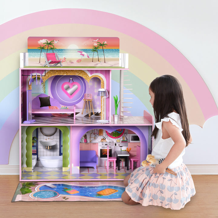 A girl is playing with Olivia's Little World Kids Wooden Dreamland Sunset 3-Level Dollhouse Set, complete with accessories, in front of a rainbow.