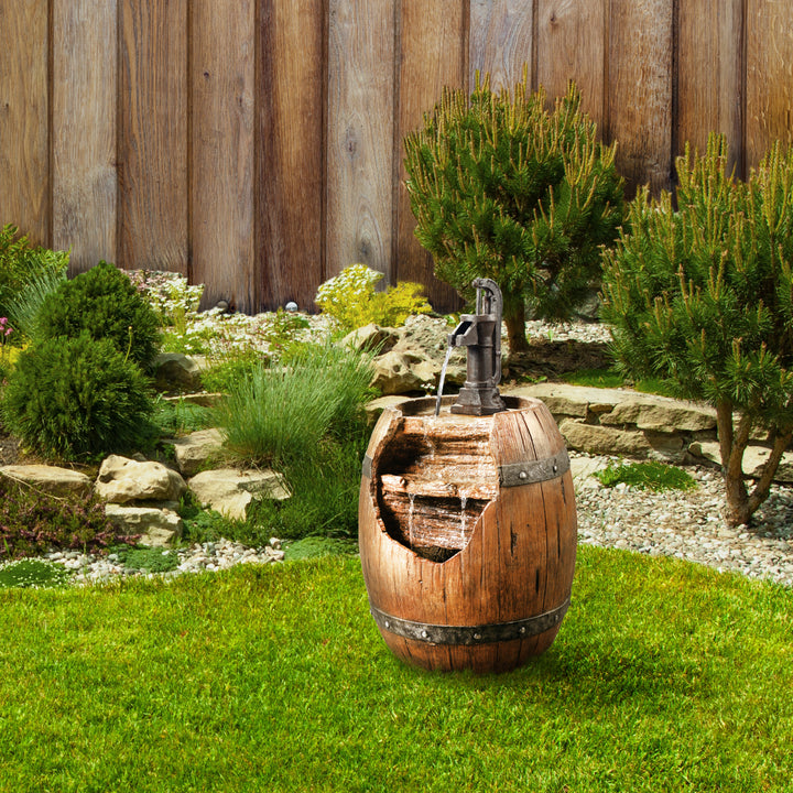 A Teamson Home Vintage Pump & Barrel water fountain in a garden setting with shrubbery and a fence