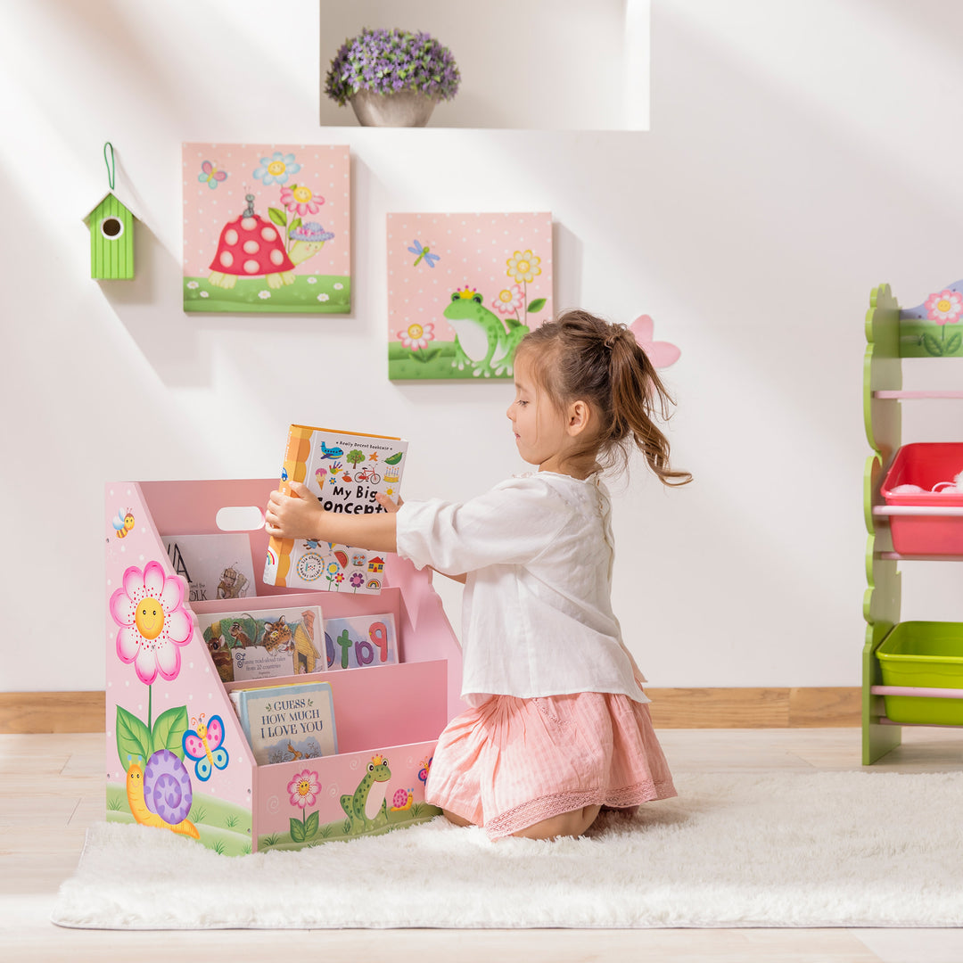 A little girl putting a book in a Fantasy Fields Kids Painted Wooden Magic Garden 3-Tiered Bookshelf, Pink in the playroom.