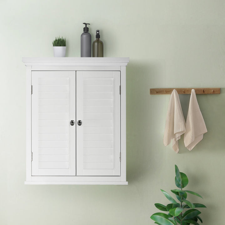 Teamson Home White Glancy Wall Cabinet with Louvered Doors with towels hanging on a wooden rack to the right and a small plant on top.