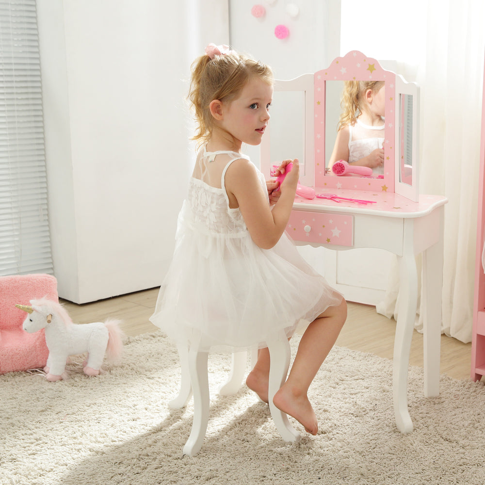A little girl in a pink dress sitting at a Fantasy Fields Gisele Play Vanity Set with Mirrors, Pink/White.
