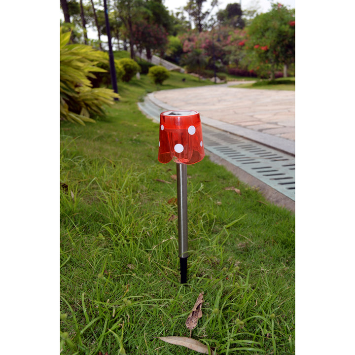 A Teamson Home Mini Solar Stake Light, red with white polka dots, on a ground spike, planted into the ground next to a pathway