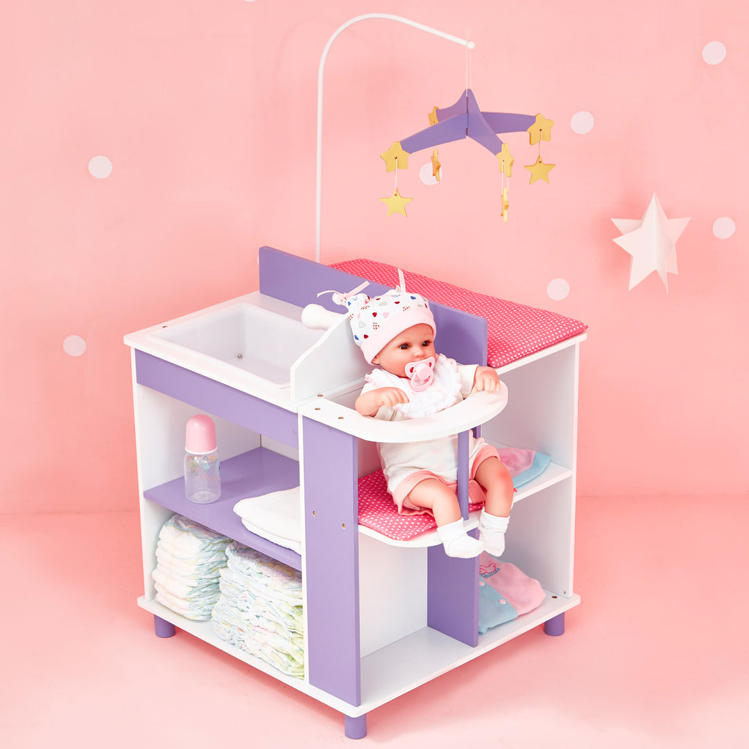 A view of the baby doll changing station in a pink room with items on the storage shelves and a baby doll sitting in the high chair.