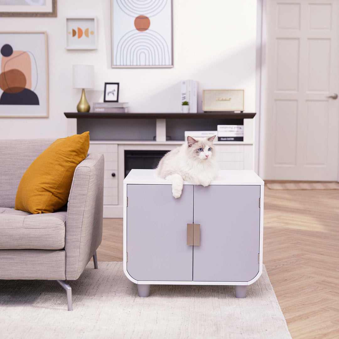 Teamson Pets Dyad Wooden Cat Litter Box Enclosure and Side Table, Alpine White, staged as an end table next to a sofa, with a white cat on top.