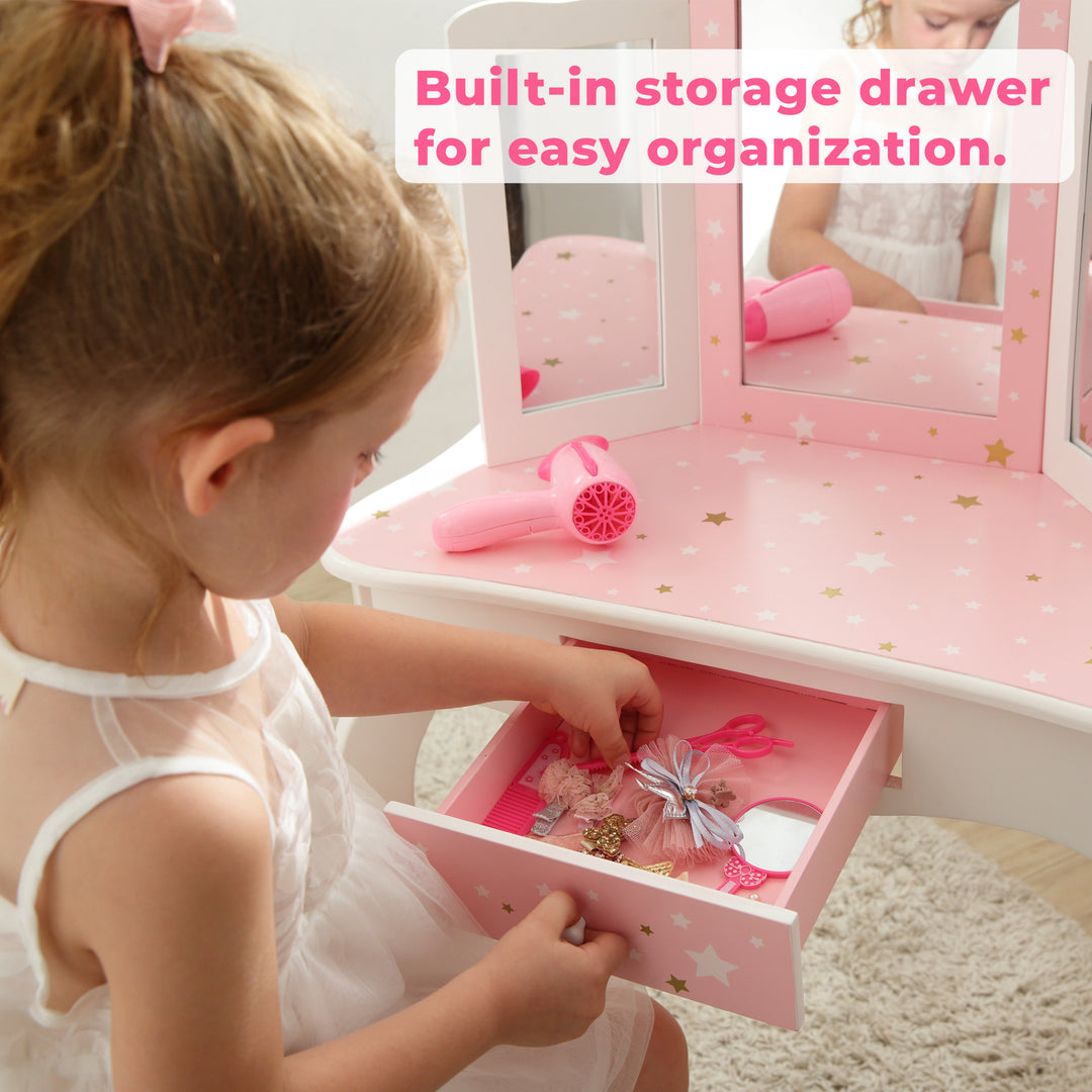 A little girl is holding a TEAMSON KIDS pink dresser with Fantasy Fields Gisele Play Vanity Set with Mirrors, Pink/White drawers.