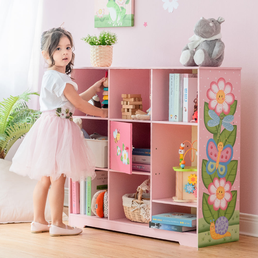 A little girl standing in front of a Fantasy Fields Kids Painted Wooden Magic Garden Adjustable Cube Bookshelf, Pink.