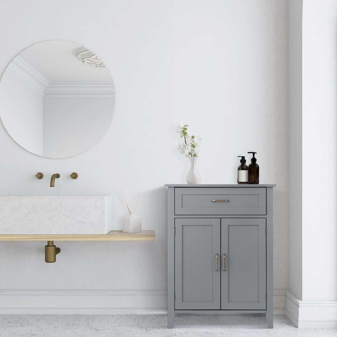 A white modern bathroom with a Mercer floor cabinet in gray with brass pull handles on the cabinet doors and top drawer