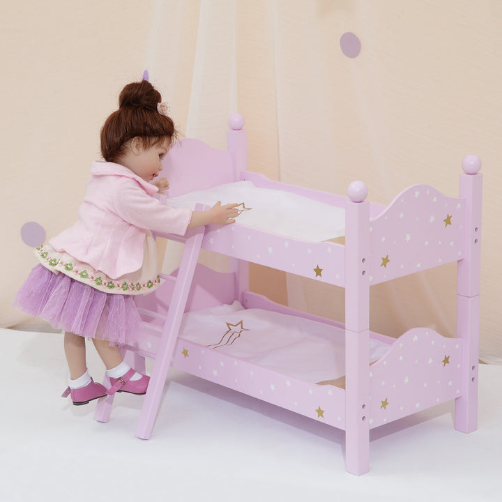 A doll standing on the ladder next to a 18" doll bunk bed pink with white and gold stars, gold pillows with white blankets.