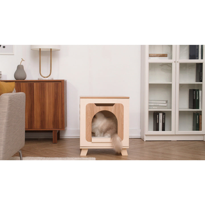 A cat partially hidden inside a Teamson Pets Elyse Elevated Vented Wooden Cat Litter Box Enclosure Side Table with its tail sticking out in a modern living room.