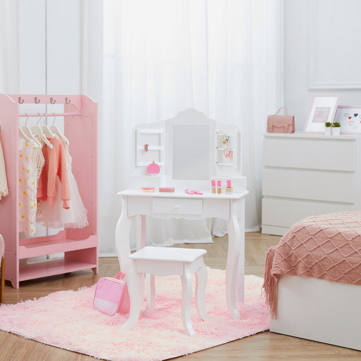 A white vanity set with matching stool, storage drawers, and a mirror with storage racks on either side in a pink and white bedroom with a pink wardrobe with dresses hanging and a bed with a pink blanket on it.