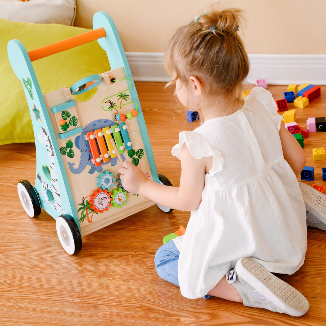 A young child playing with a Teamson Kids Preschool Play Lab Wooden Baby Walker and Activity Station on the floor.