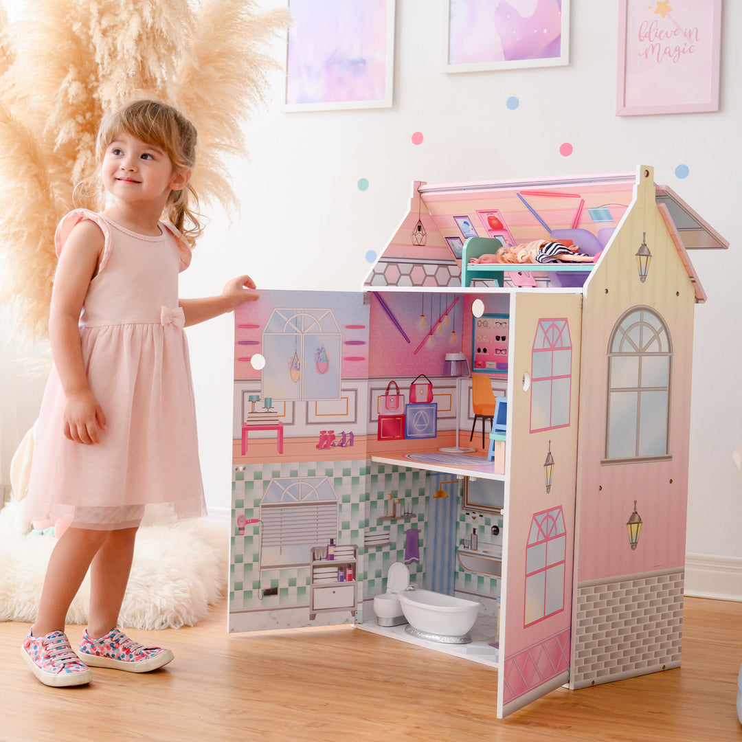 A little girl standing in front of Olivia's Little World Dreamland Glass-Look Dollhouse for 12" Dolls, Multi-Color with accessories.