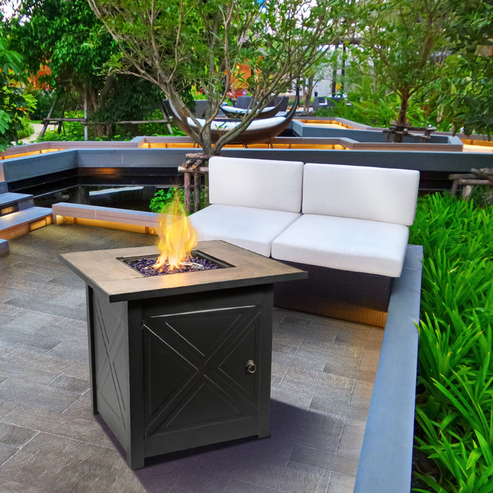Teamson Home Outdoor Square 30" Propane Gas Fire Pit with Steel Base, Black and modern white sofa surrounded by greenery.