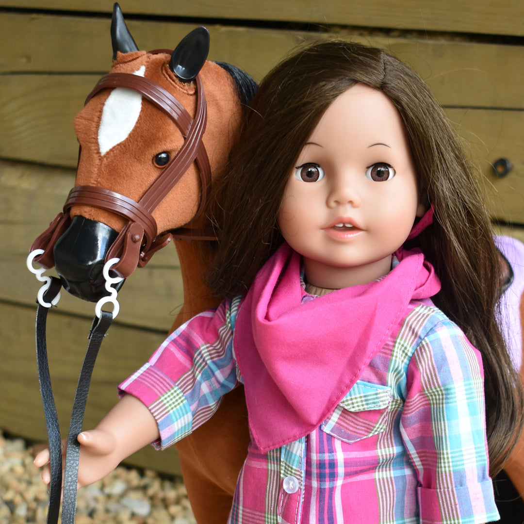 An 18" brunette doll holding the bridle of her brown horse.