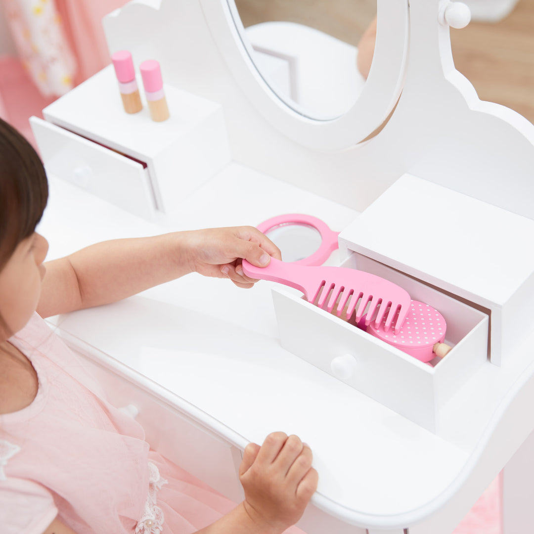 A little girl is putting a pink comb away in a storage drawer on her white vanity table.