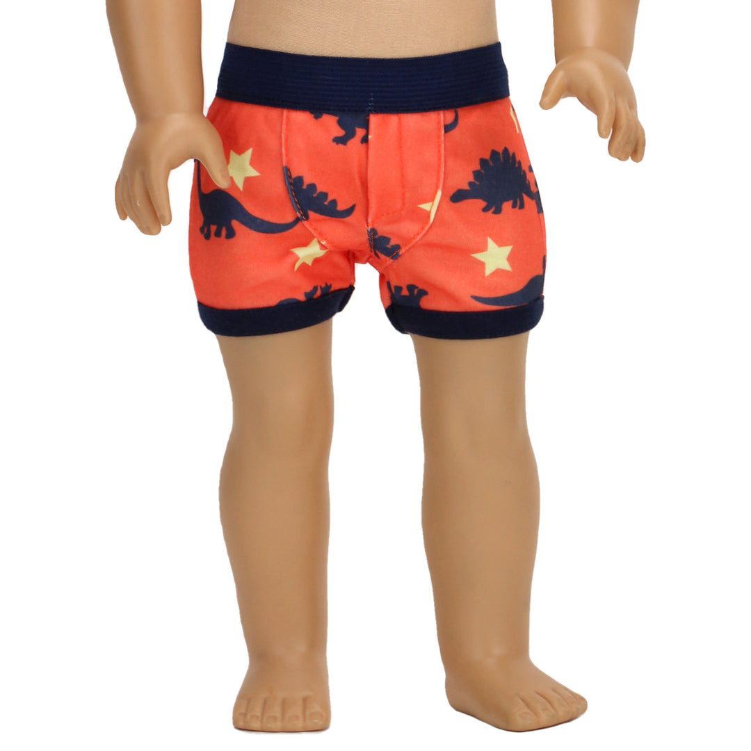 Lower half of a Sophia's 18" boy doll standing with a pair of orange underpants on with navy dinosaurs and yellow stars on them.