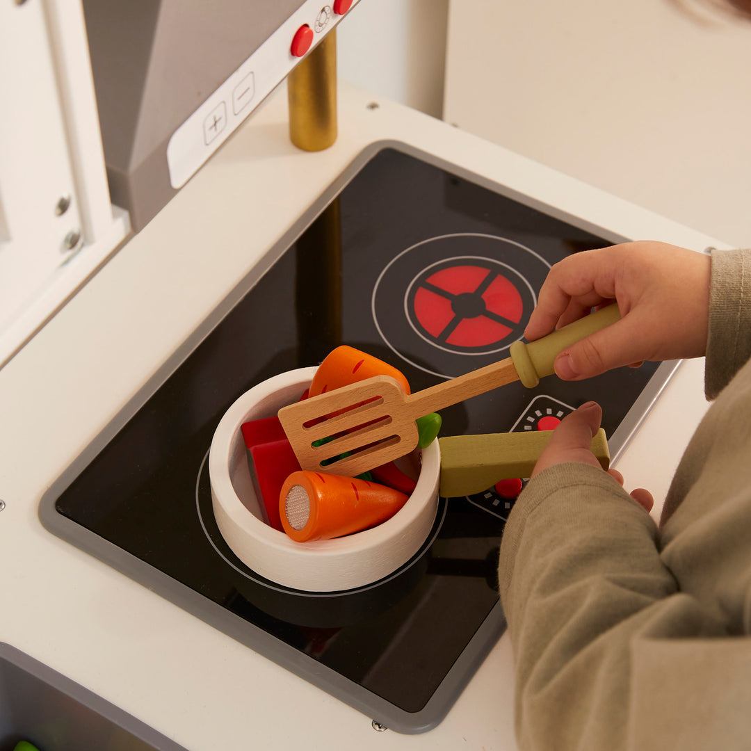 Child pretend cooking on the play stovetop, cooking wooden vegetables with a spatula. 