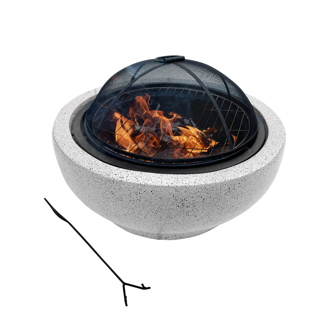 A Teamson Home Outdoor 24" Wood Burning Fire Pit with Grill Grate and Faux Concrete Base, Gray with a fire burning under a mesh spark screen with a poker next to it