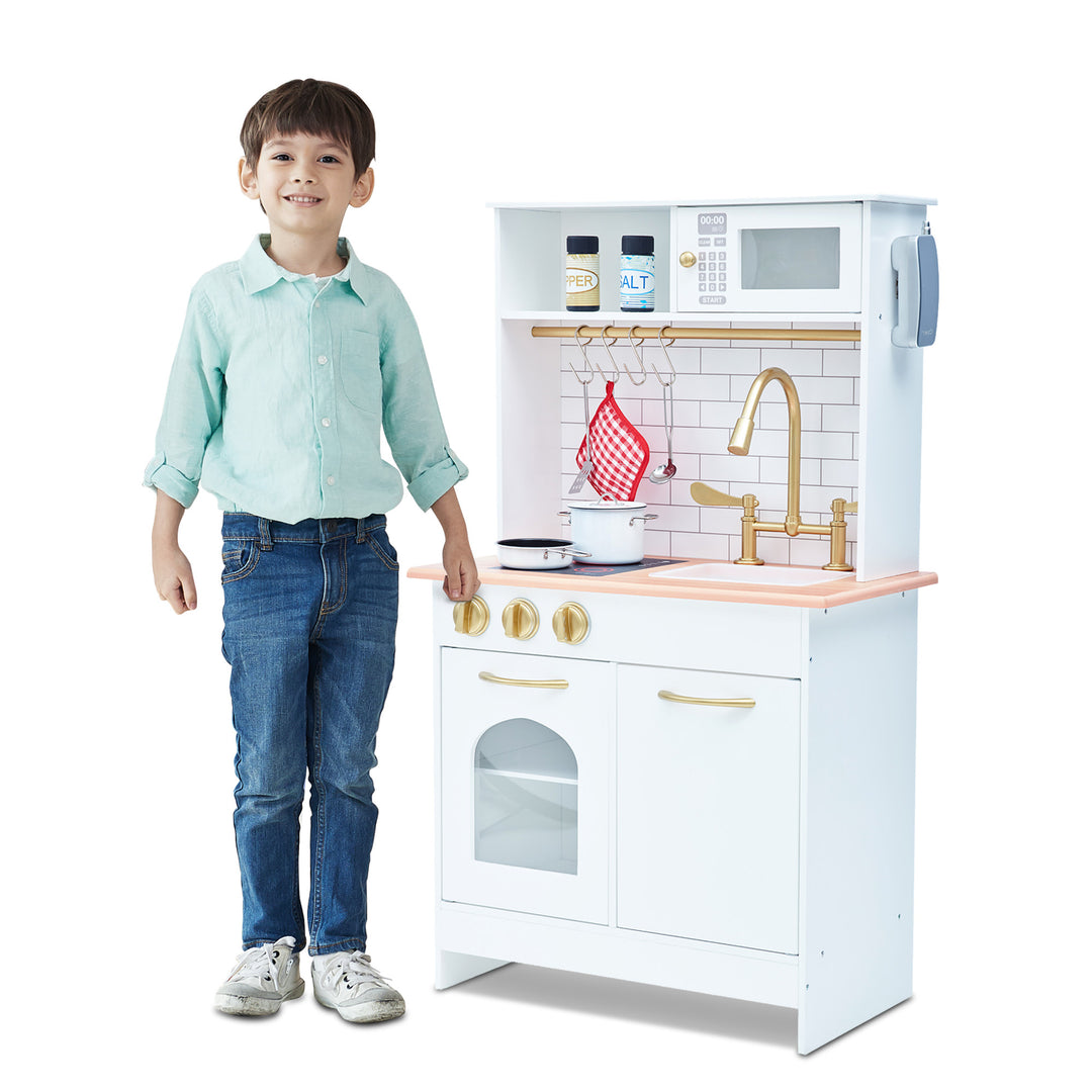 Young boy standing next to a Teamson Kids Little Chef Boston Classic Play Kitchen & Cookware, White.