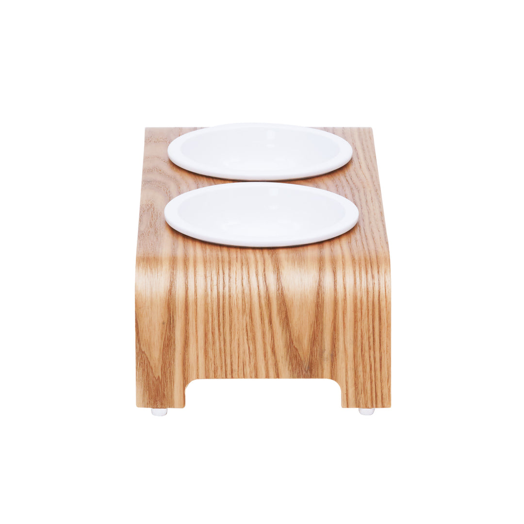 A view from the side of the Billie Small Elevated Ash Wood Pet Feeder with white ceramic bowls and a wood grain finish.