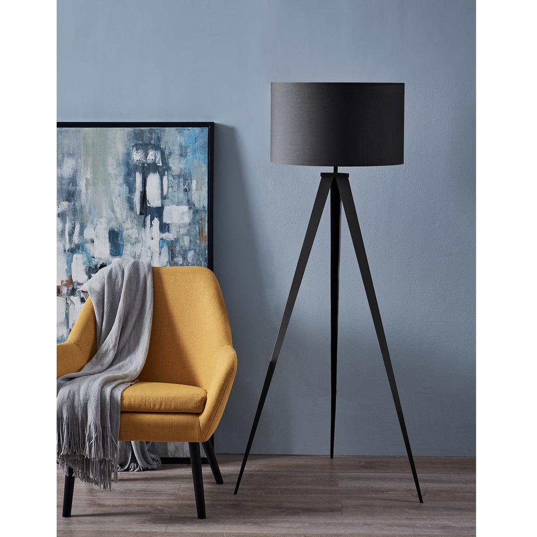 Modern living room corner with a yellow armchair, gray throw blanket, Teamson Home Romanza 60" Postmodern Tripod Floor Lamp with Drum Shade, Matte Black, and abstract painting against a blue wall.