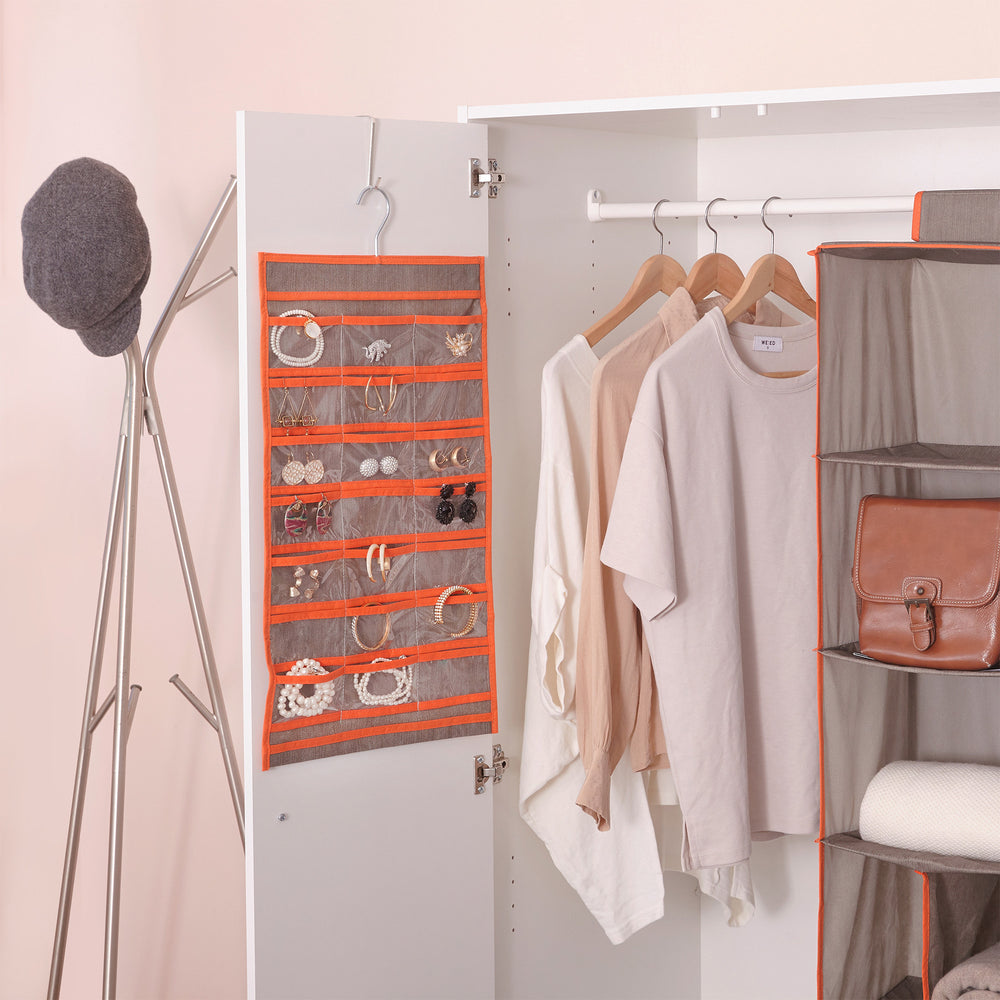Teamson Home 21-Pocket Hanging Jewelry Organizer, Gray with Orange Trim hung on a hook over a closet door with necklaces and earrings in various pockets