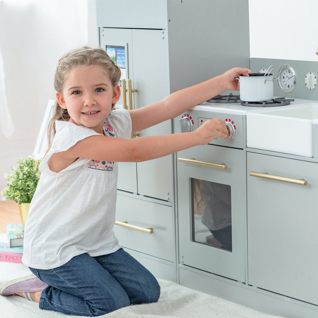 Young girl playing with a Teamson Kids Little Chef Charlotte Modern Play Kitchen, Silver Gray/Gold.