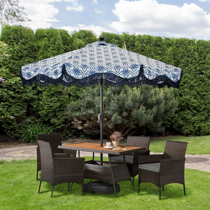 Teamson Home Outdoor Brown PE Rattan & Acacia 5-Piece Patio Dining Set with White Cushions underneath a separate patio umbrella in a yard setting with tall shrubs behind it
