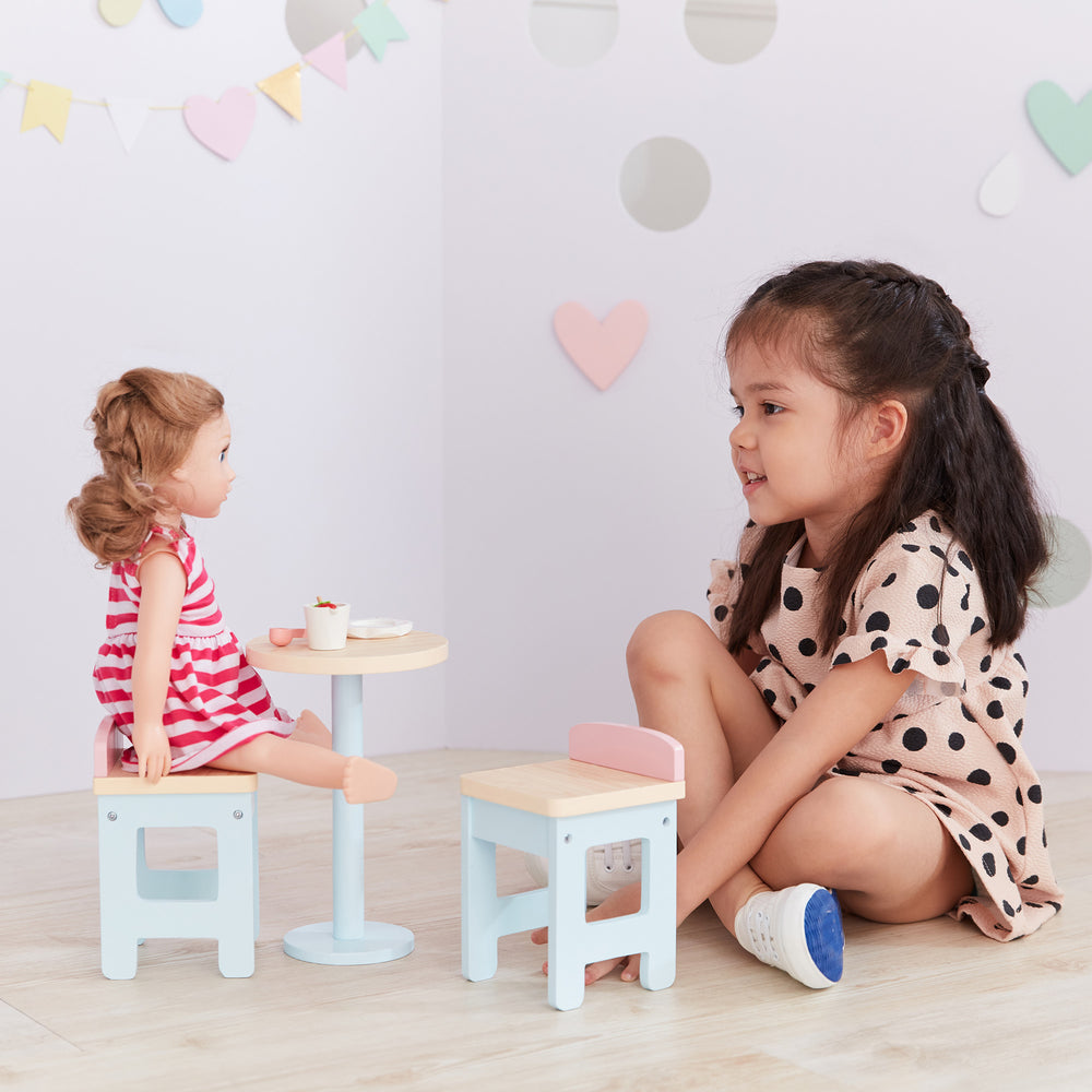 A little girl is playing with 18-inch dolls, Olivia's Little World Modern Nordic Princess Roundtable and 2 Stools.
