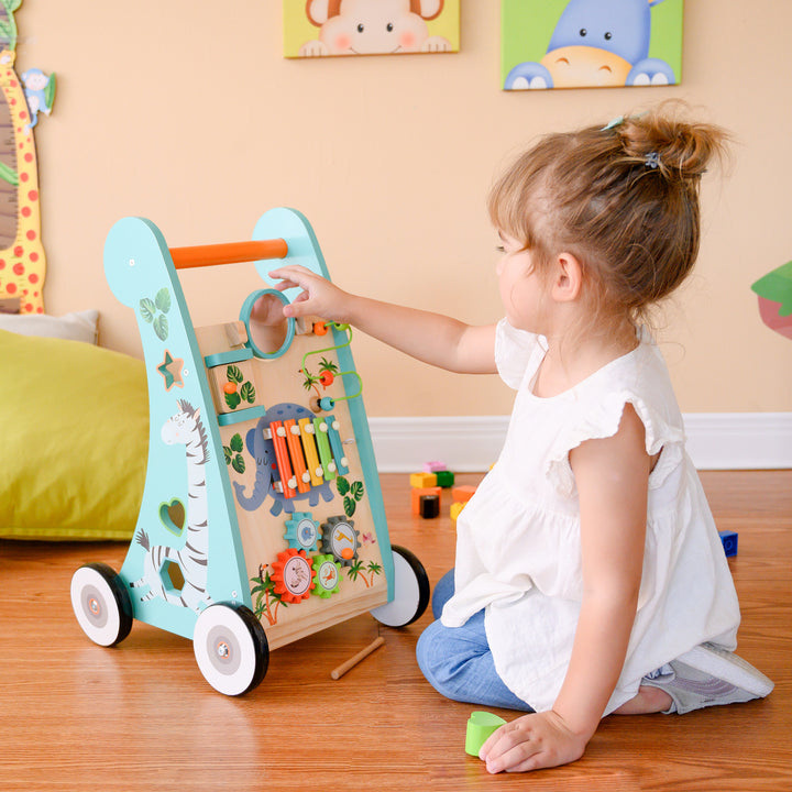 A young child playing with a Teamson Kids Preschool Play Lab Wooden Baby Walker and Activity Station, looking in the mirror.