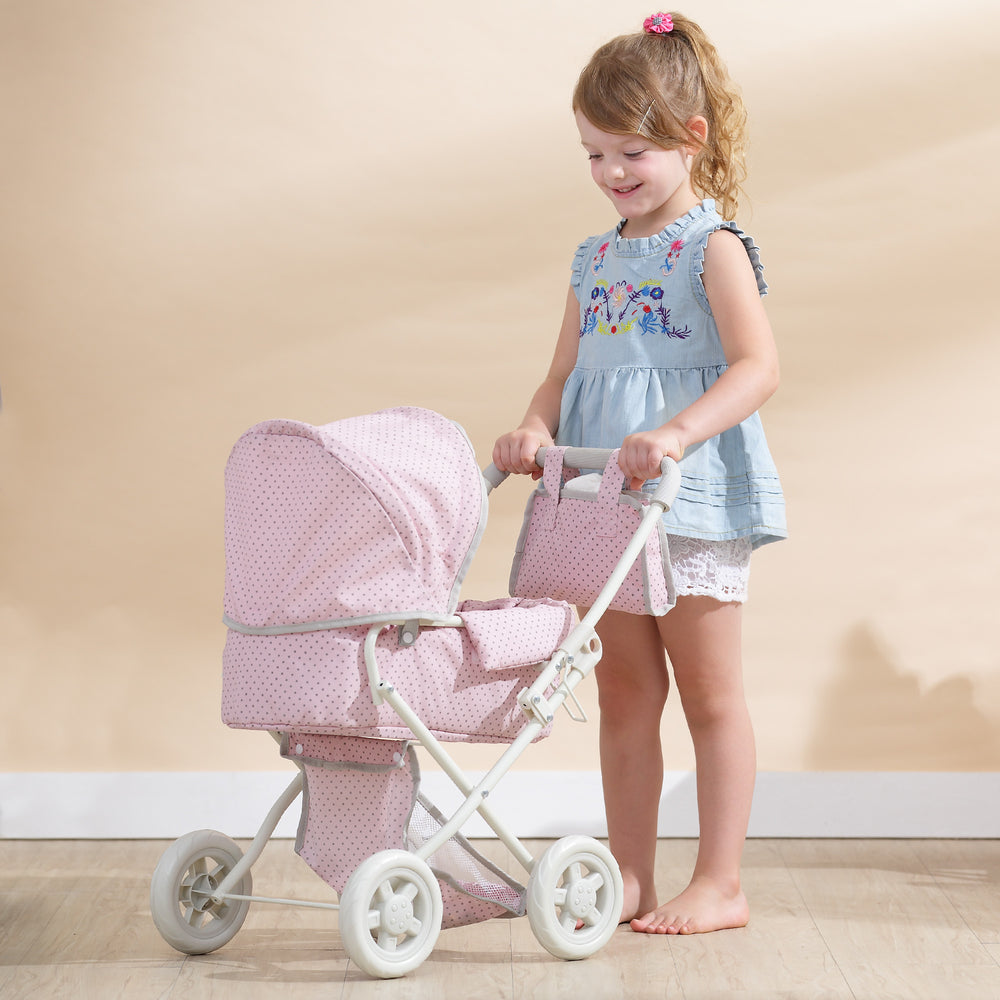 A little girl is standing next to Olivia's Little World Polka Dots Princess Deluxe Baby Doll Stroller in pink for her baby doll.