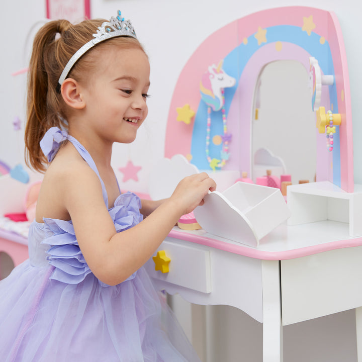 A little girl in a lavender dress opening a cloud-shaped drawer at her rainbow and white vanity table.
