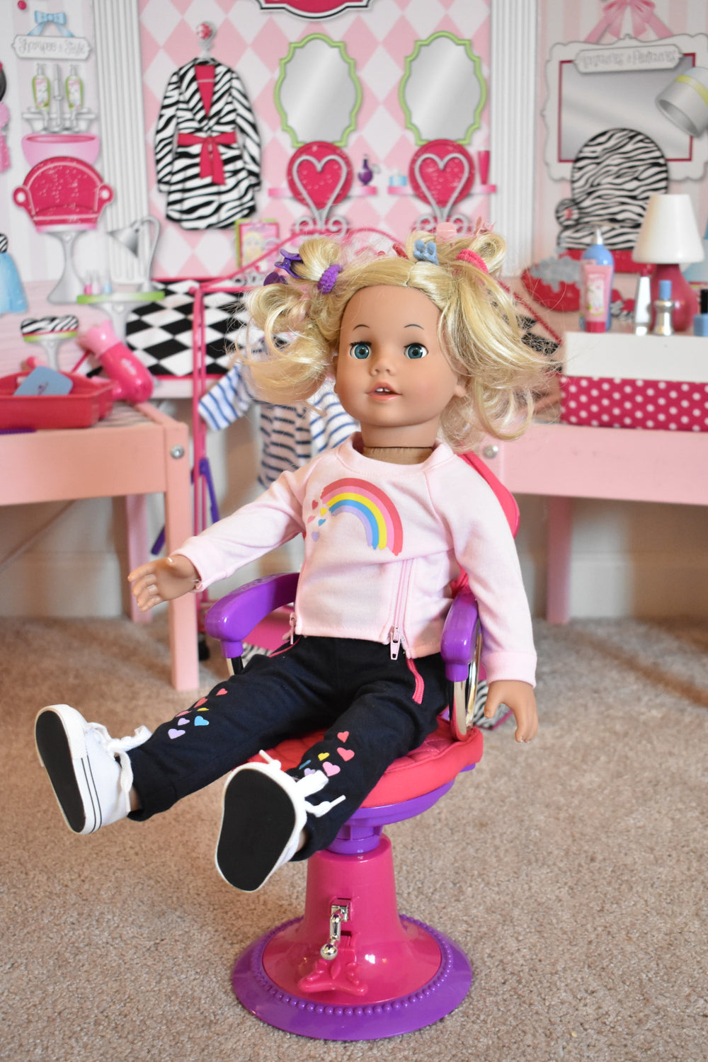 An 18" blonde doll sitting in a salon chair with a salon background behind her.
