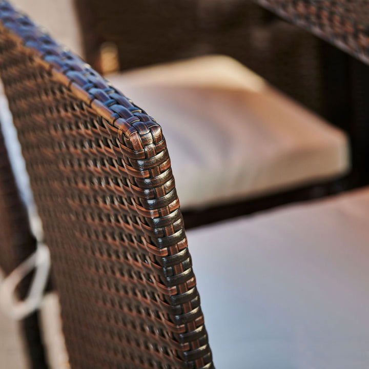 Close-up of a Teamson Home 5 Pc Outdoor Wicker Dining Set armrest with a cushioned seat in the background.