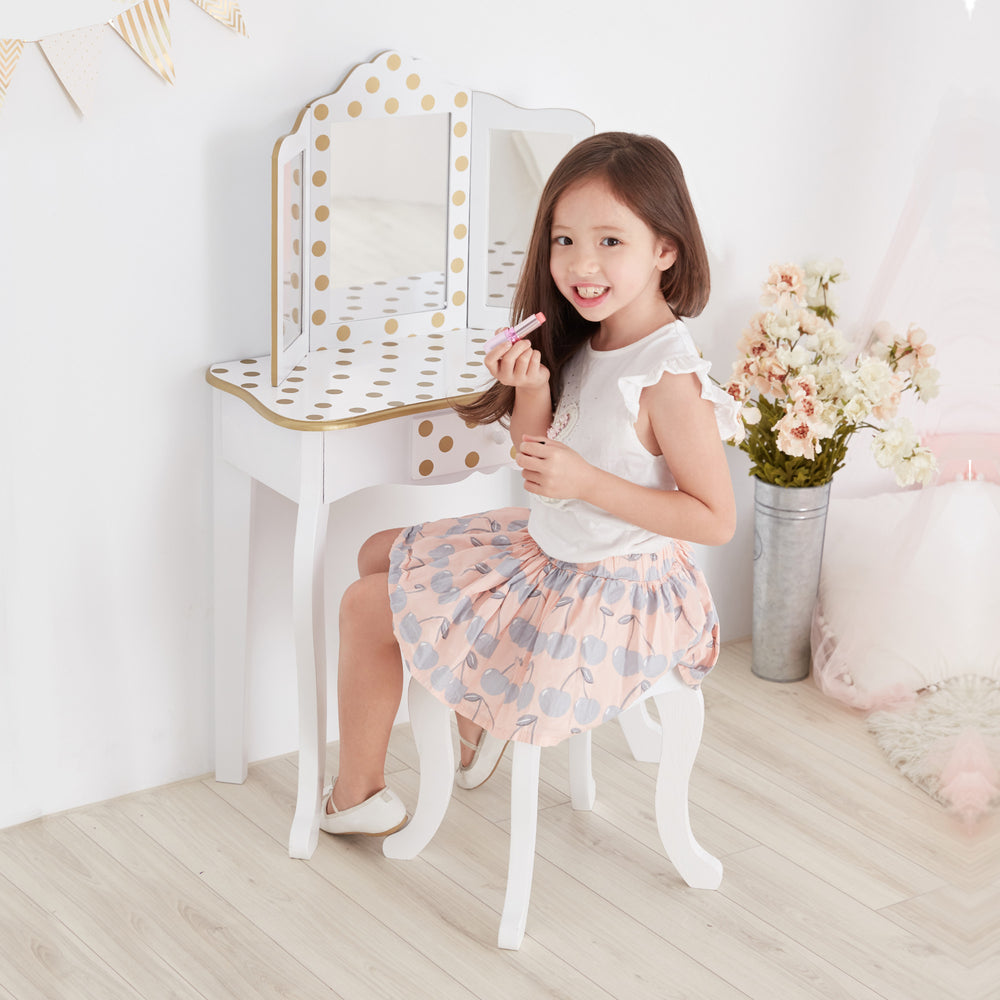A little girl sitting on a Teamson Kids Gisele Polka Dot Vanity Playset chair in front of a Fantasy Fields mirror.