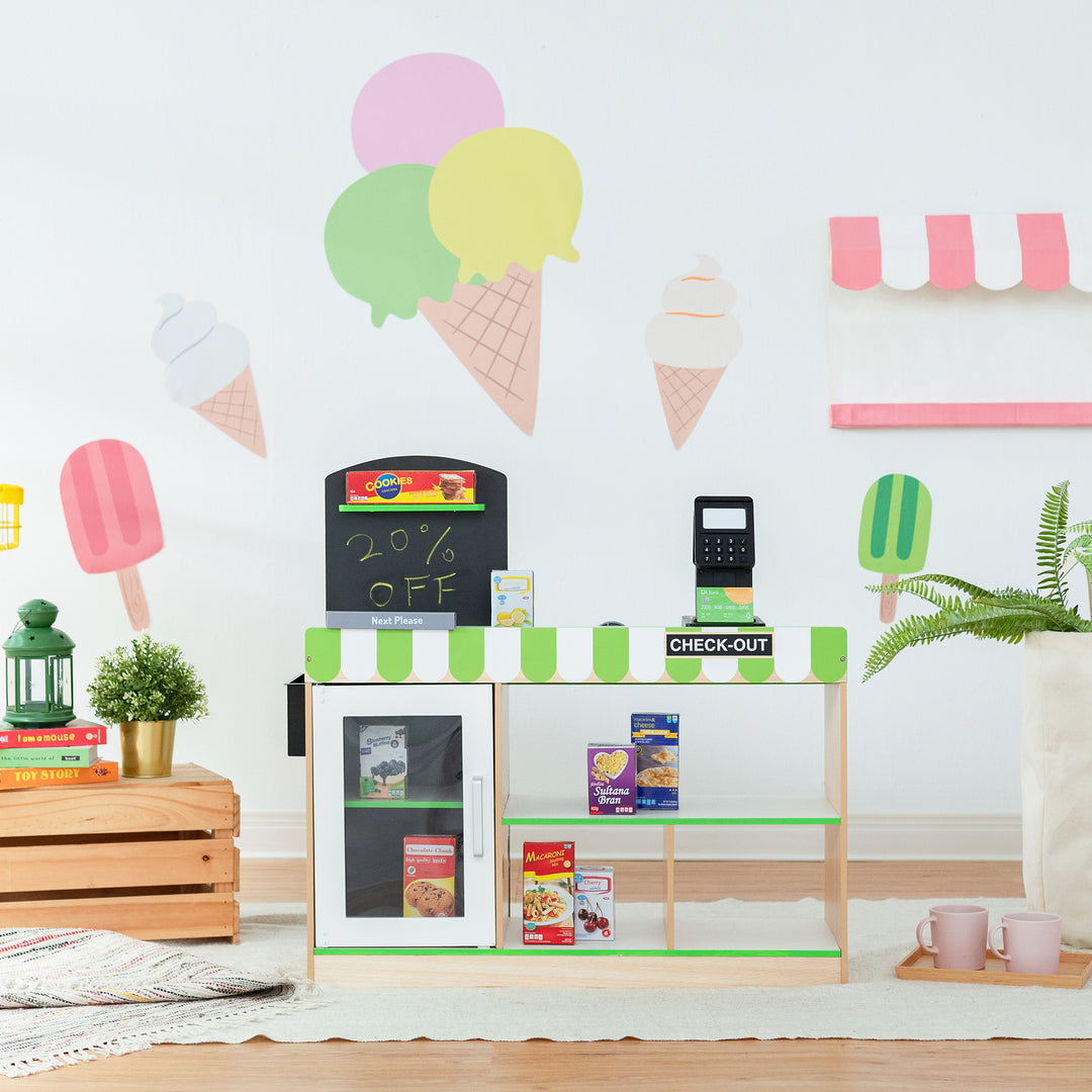 Child's playroom set up as a pretend ice cream shop with colorful decorations and a Teamson Kids Cashier Austin Play Market Checkout Counter with 26 Accessories, Green/Natural.