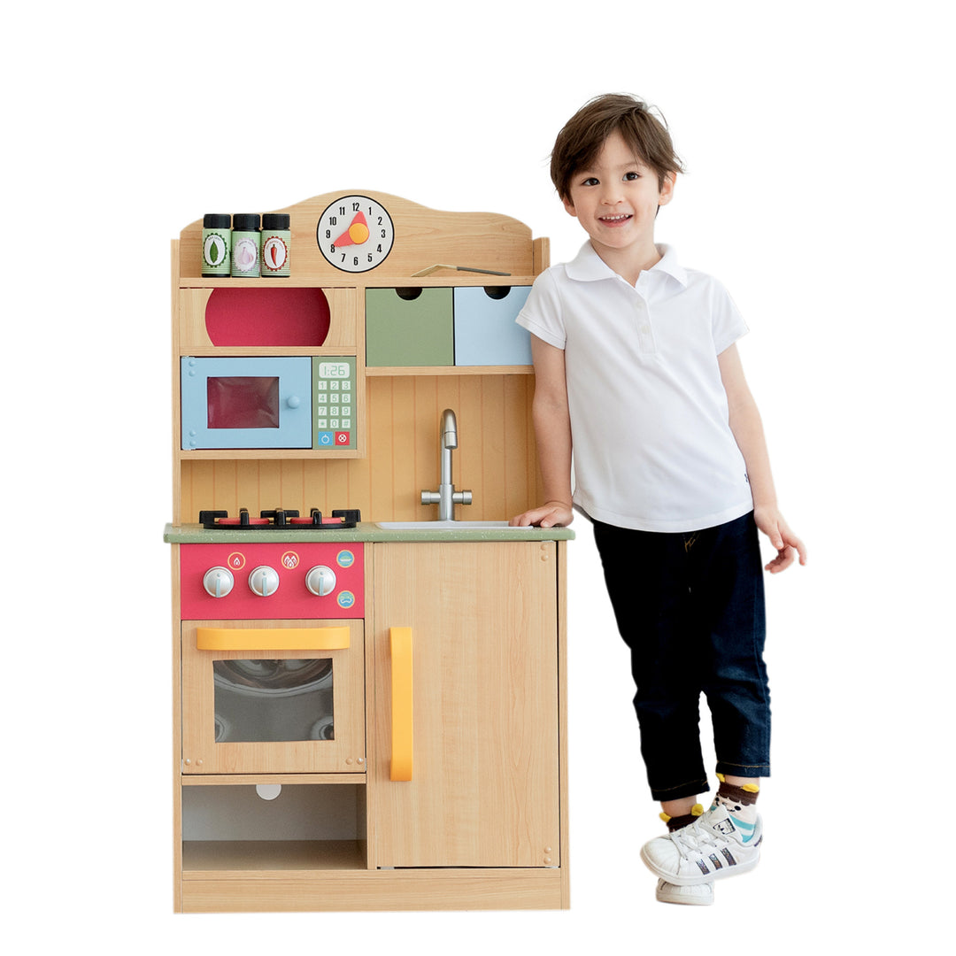 Boy leaning next to the Teamson Kids Little Chef Florence Classic Play Kitchen with 5 Kitchen Accessory Toys, Wood Grain