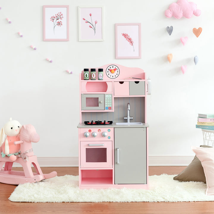A pink and gray Teamson Kids Little Chef Florence Classic Play Kitchen with accessories in a room decorated with pastel wall art and plush toys.