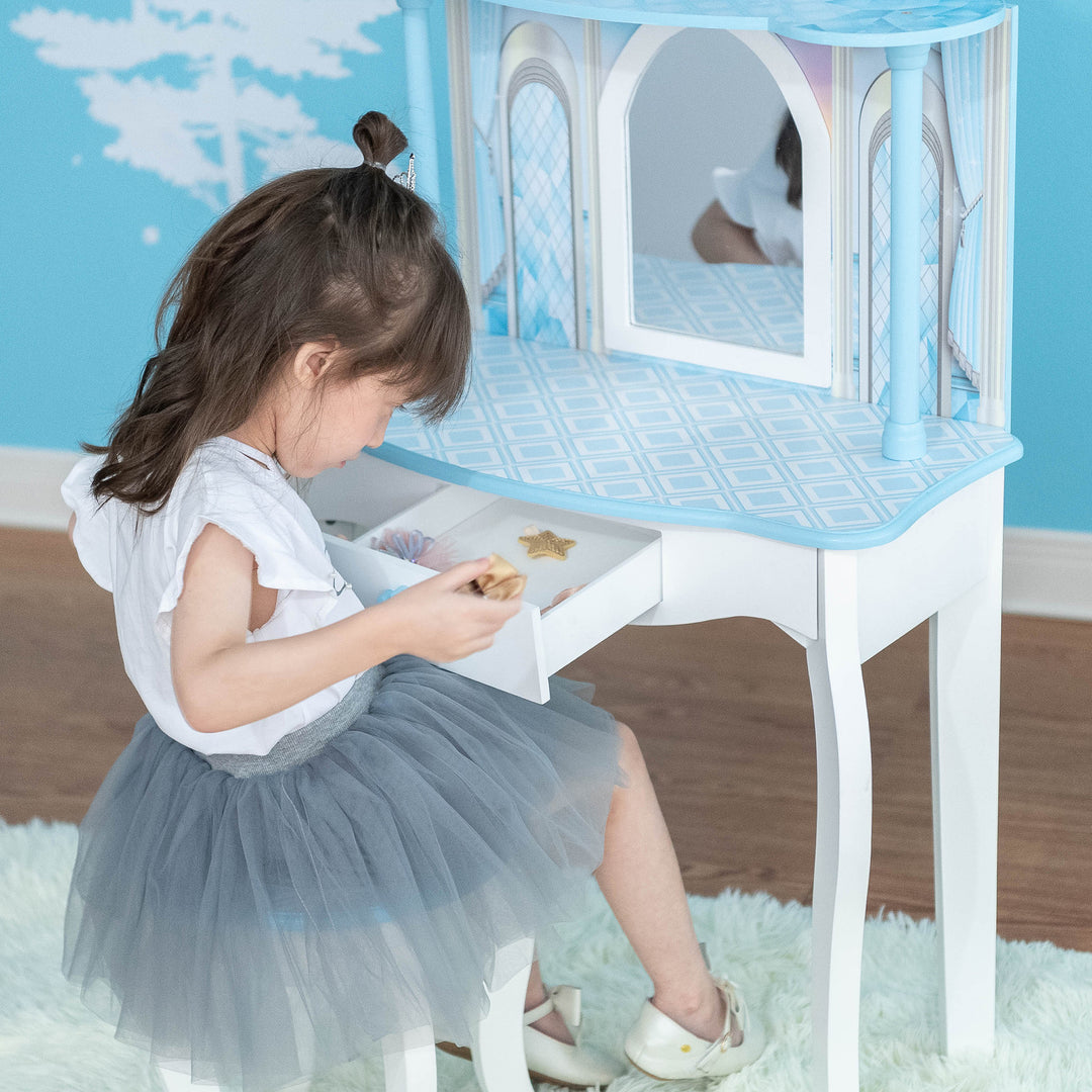 A little girl is sitting at a table with a blue and white Fantasy Fields Kids Dreamland Castle Vanity Set with Chair and Accessories.