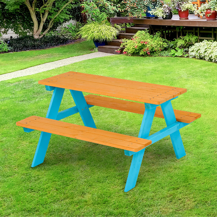 A versatile Teamson Kids Child Sized Wooden Outdoor Picnic Table with aqua legs and a warm honey tabletop, set on a grass lawn in a garden.