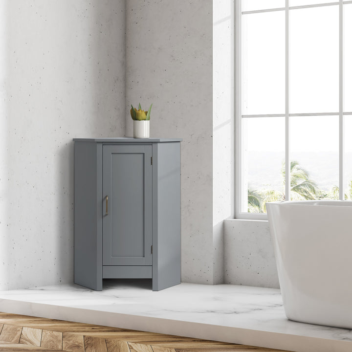 A Teamson Home Mercer Mid Century Modern Gray Corner Floor Storage Cabinet in a white marble bathroom next to a window in a bathroom