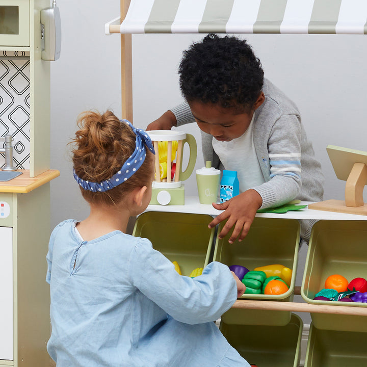 Two children play together at the Teamson Kids Little Chef Frankfurt Wooden Blender Play Kitchen Accessories, Green, organizing pretend ingredients and food items.