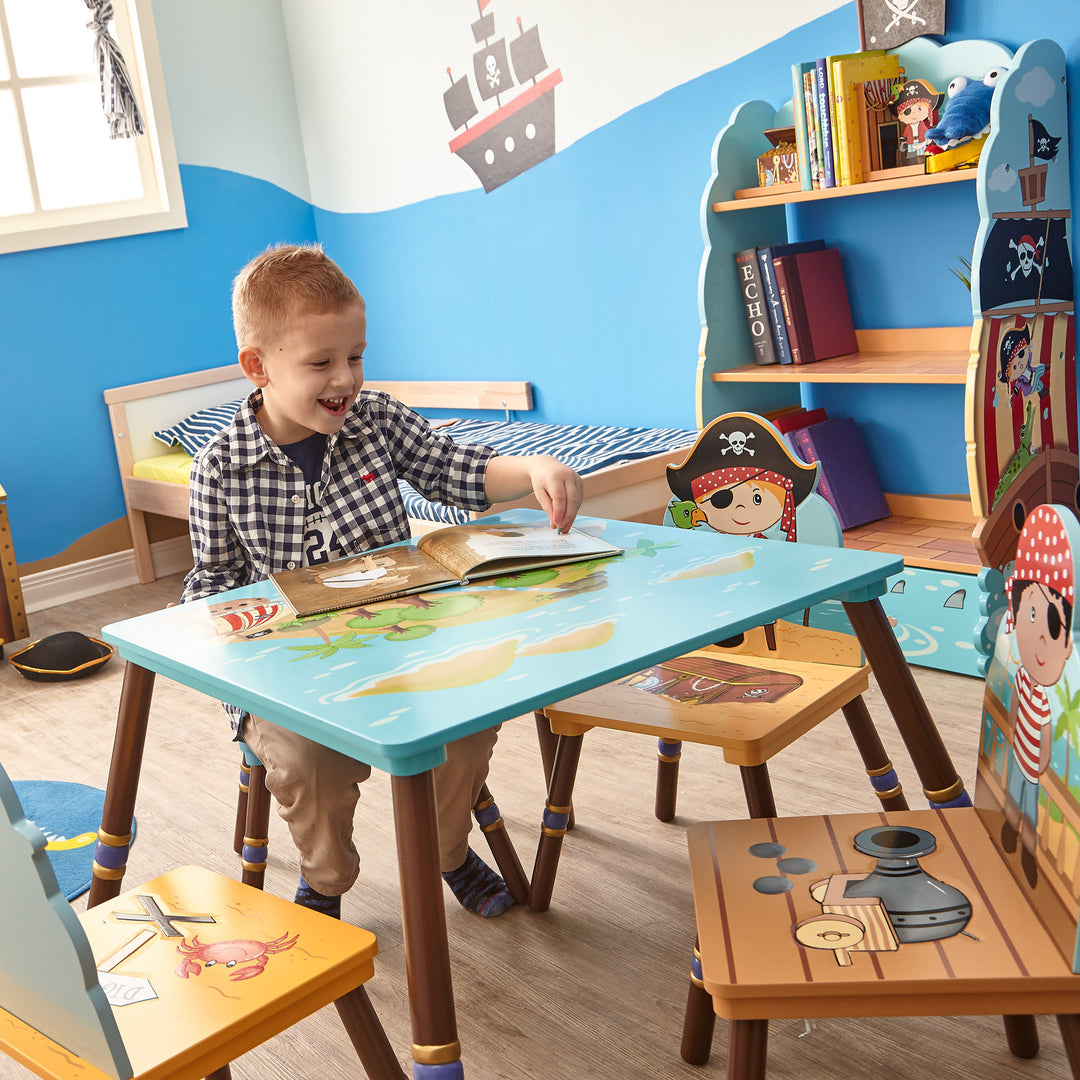 A little boy sitting at a child-sized pirate-themed table in a room full of pirate-themed chairs, shelving and wall hangings.