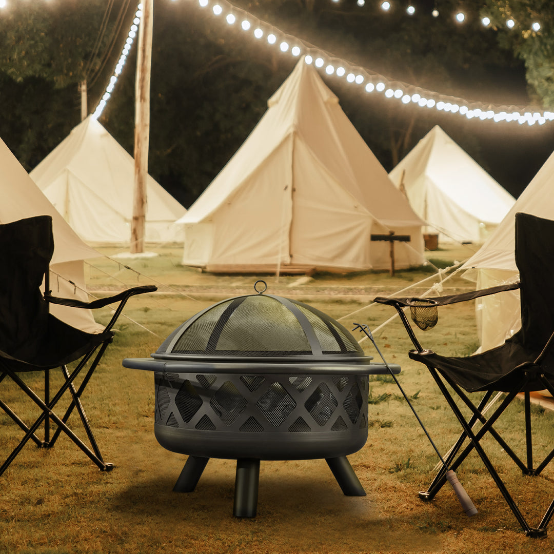 A cozy glamping site at twilight with lit string lights and a Teamson Home 30" Outdoor Round Wood Burning Fire Pit with Steel Base, Black, ready for an evening outdoors.