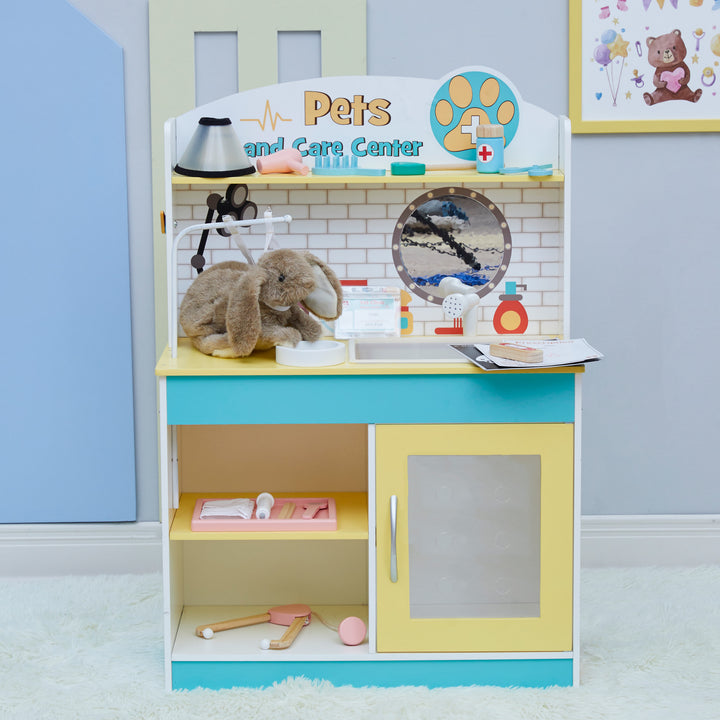 A Teamson Kids Little Helper Wooden Pet Care and Veterinary Clinic Playset with various pretend vet exam accessories and a plush bunny on top.