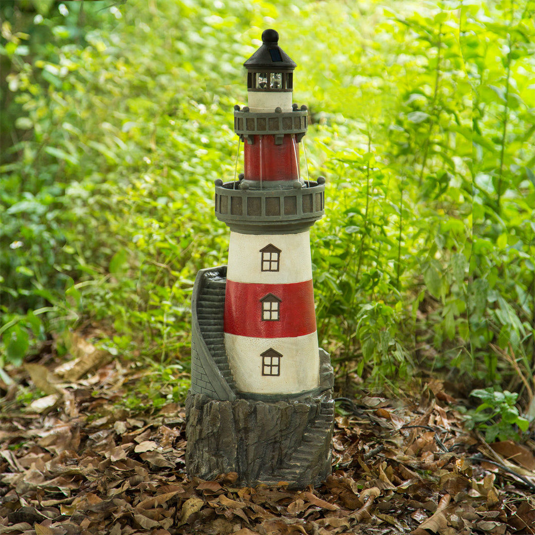Teamson Home Lighthouse Outdoor Solar Fountain with Rotating LED Light, Red/White, in a wooded setting
