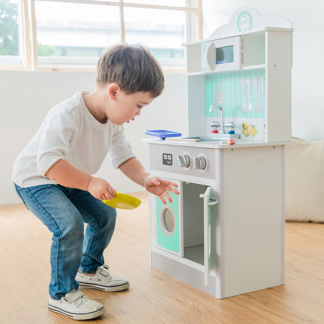 Boy putting a pretend plate into the oven door of the Teamson Kids Little Chef Madrid Classic Play Kitchen with Salt & Pepper Shakers, Mint/Gray