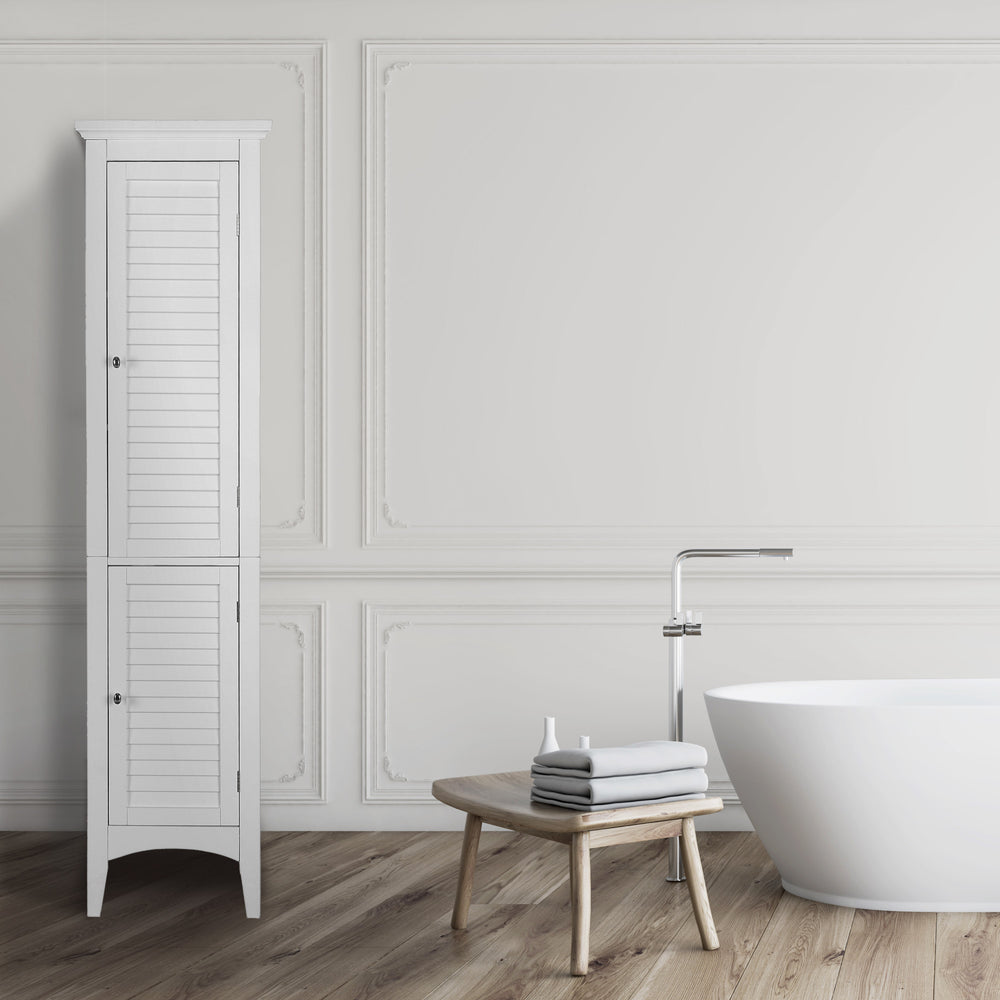 A minimalist bathroom interior with a Teamson Home Glancy Wooden Tall Tower Cabinet with Storage in White, freestanding bathtub, and a small wooden table with towels.