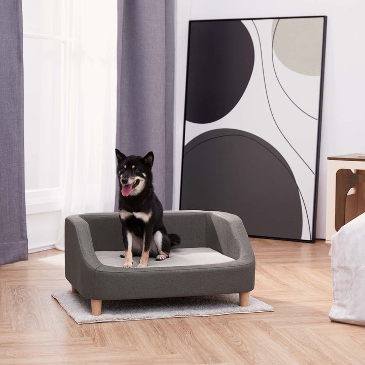 A two-tone gray Bennett Linen Sofa Pet Bed with a black and white dog sitting on it.
