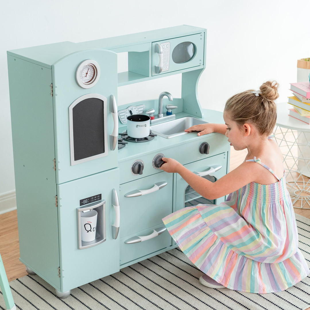 A young girl plays with a Teamson Kids Little Chef Westchester Retro Kids Kitchen Playset, Mint, complete with an interactive toy telephone.